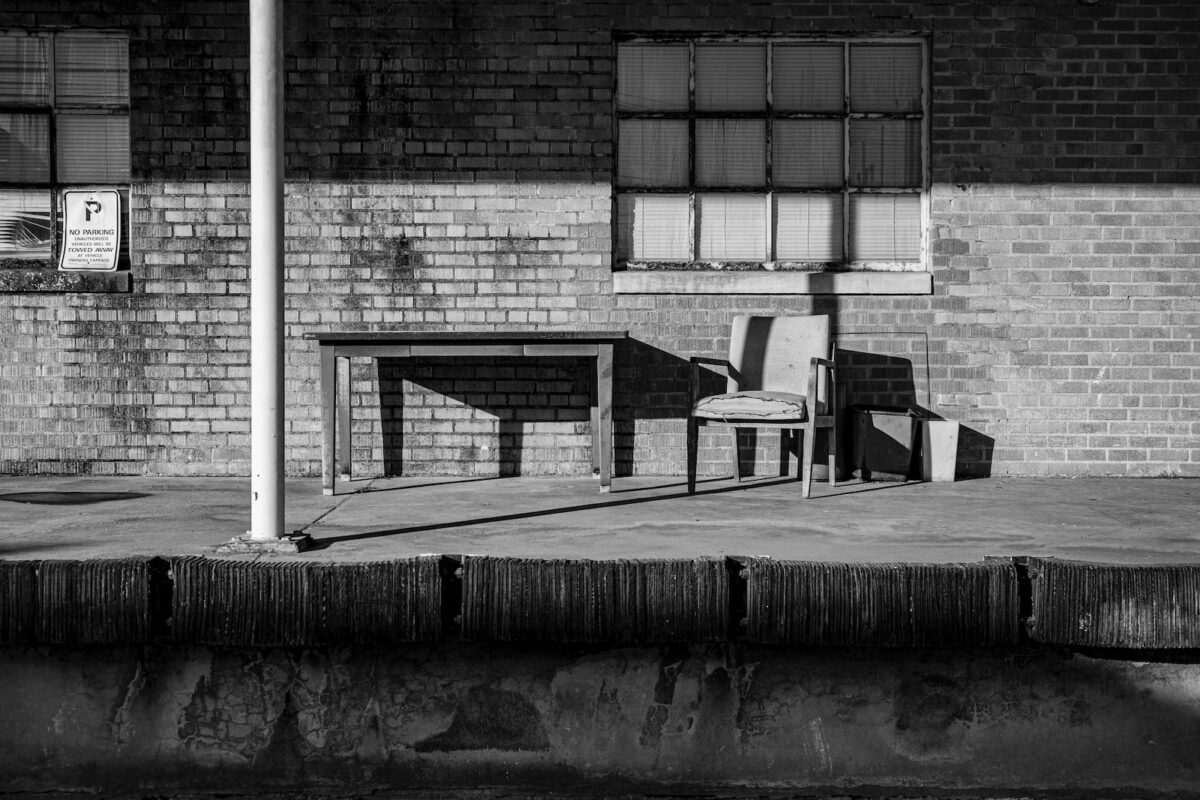 grayscale photo of wooden bench near building
